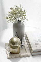 Matte neutral ceramic vase with sculptural shape styled with soft green foliage on white table