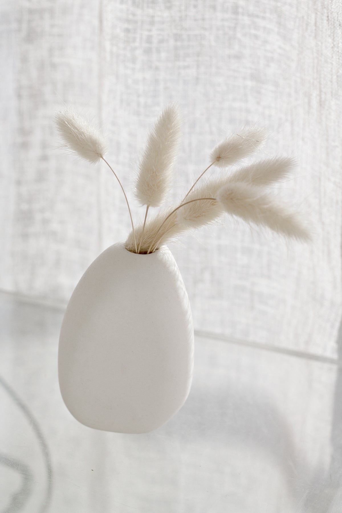 Ned Harmie Vase Pipi White matte ceramic bud vase styled with fluffy dried stems on a glass surface in soft natural light