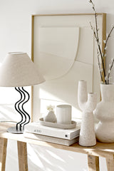 Oval Noosa dish used as a tray for a candle and small vase, styled on stacked books beside speckled sculptural vases and a curved black lamp