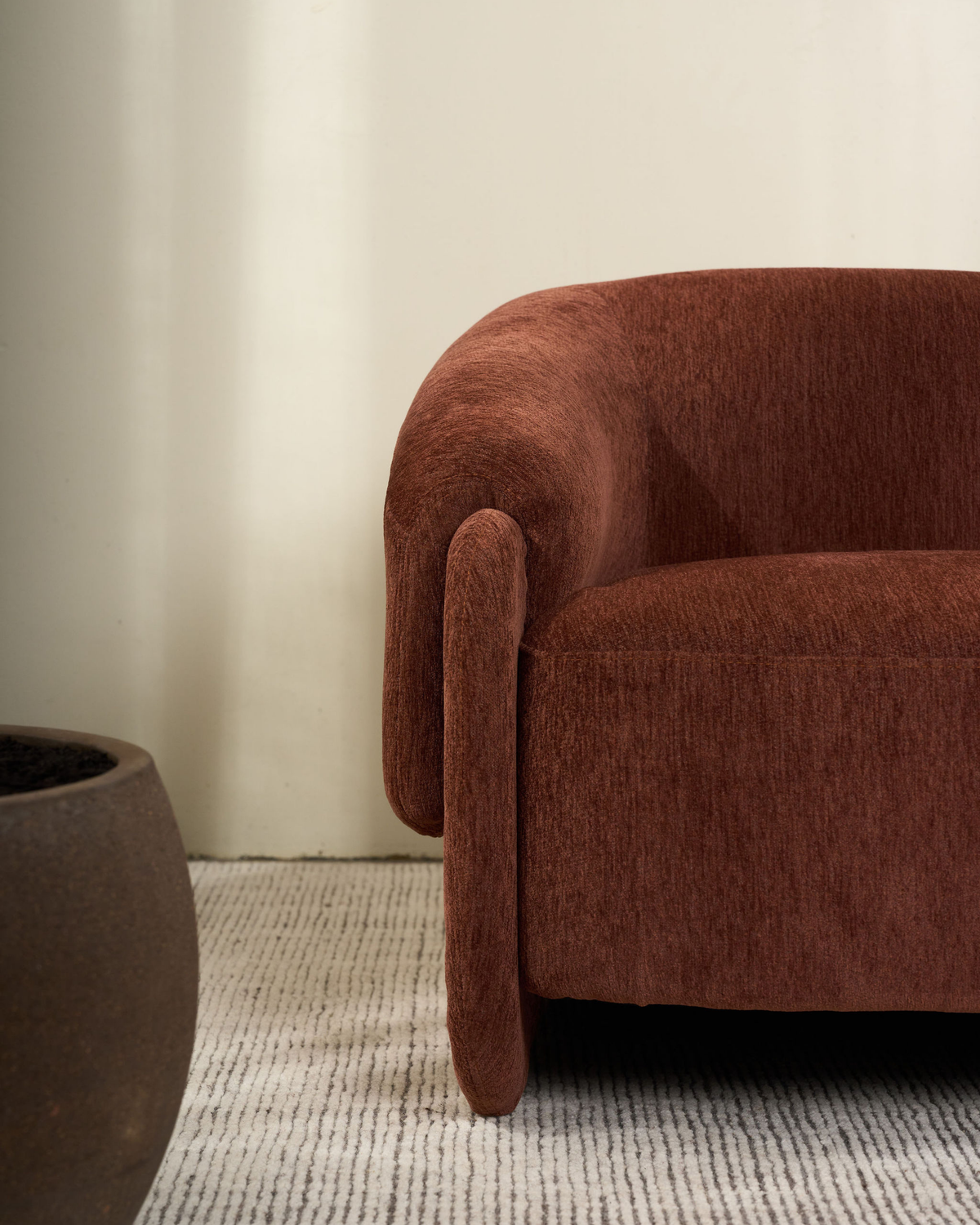 Close view of the curved arm and ribbed rust-brown upholstery beside a dark planter