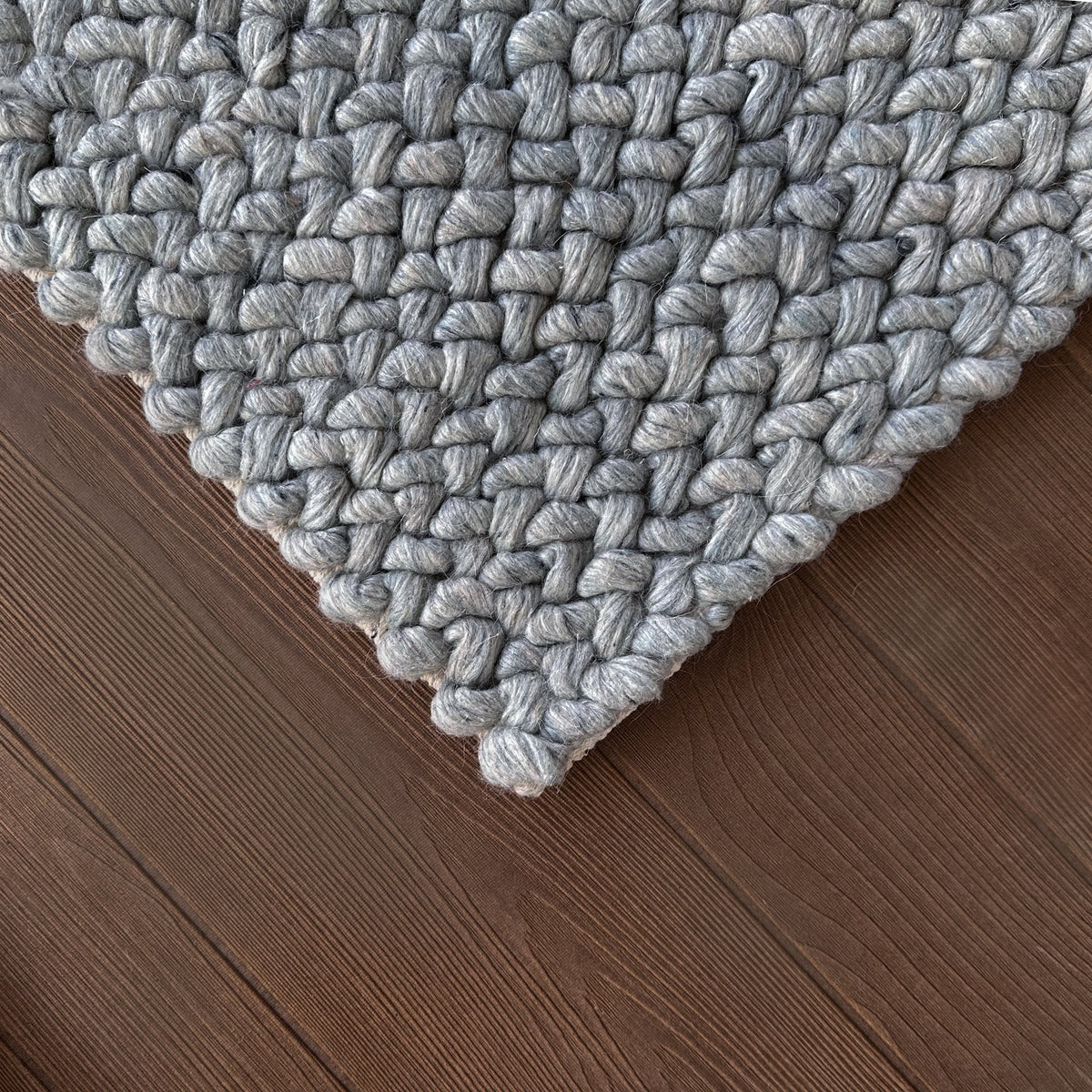 Corner of the chunky grey woven rug on a dark timber floor