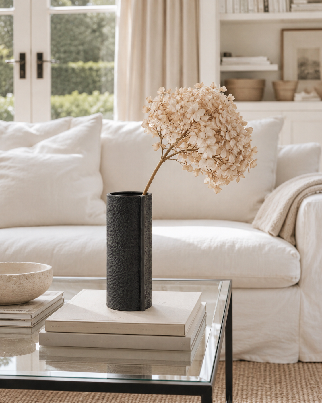 Small black Zakkia burlap vase holding a dried hydrangea stem on a glass coffee table