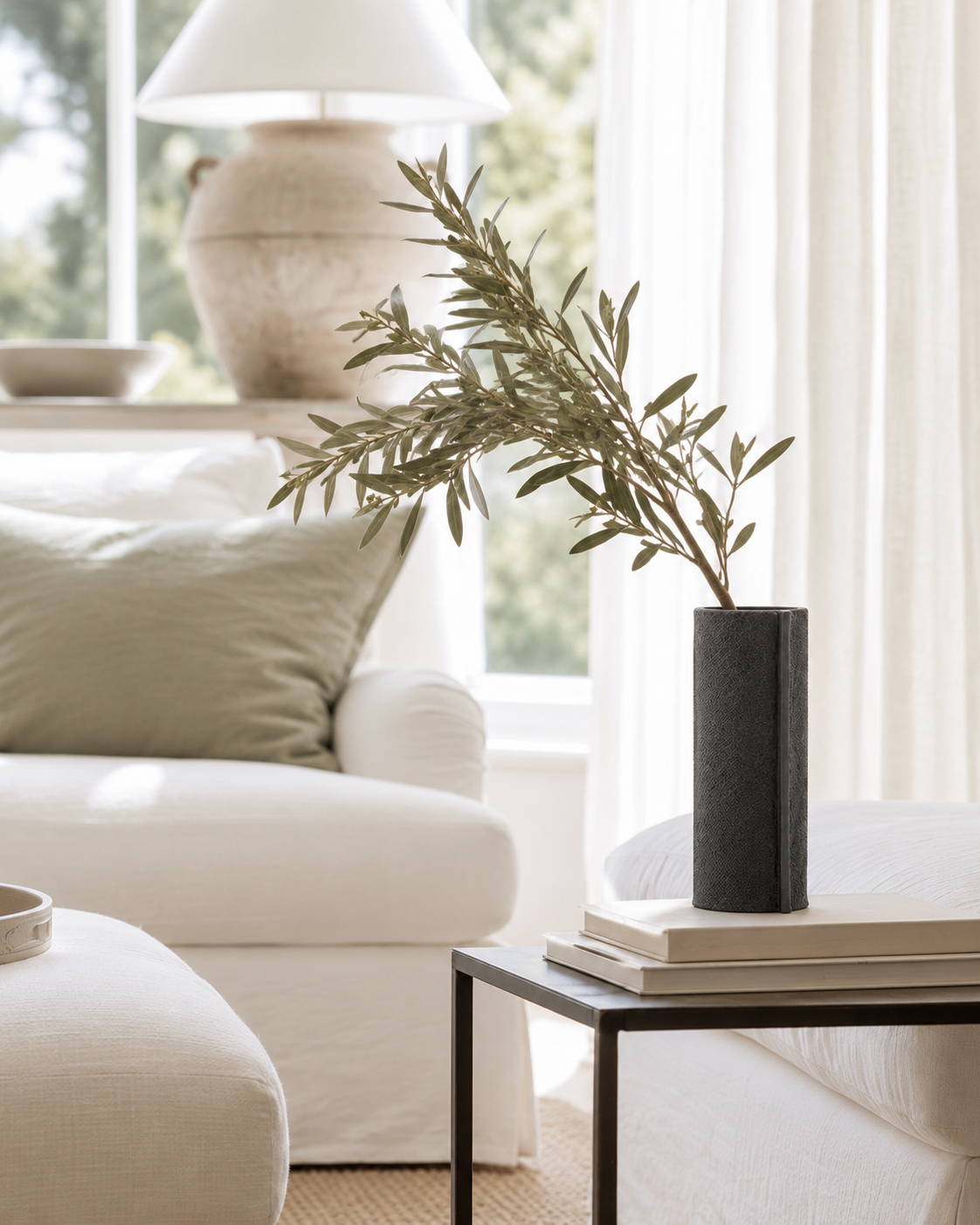 Small black Zakkia burlap vase with an olive branch on a side table beside a linen armchair