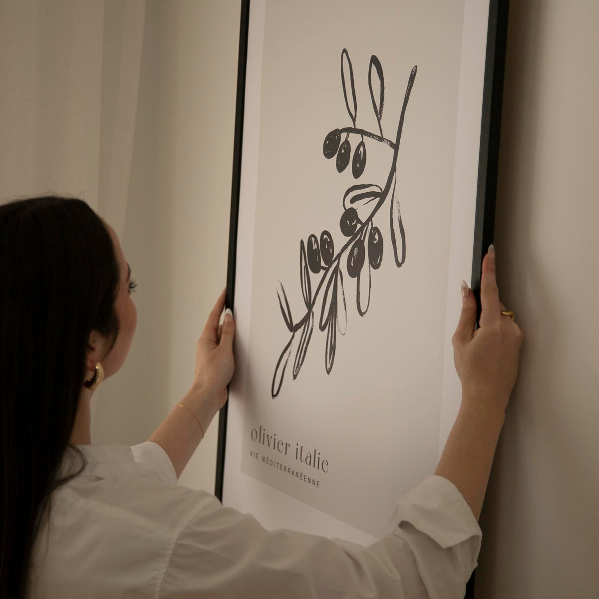 Woman holding up the Olive Tree print in a large black frame against a warm white wall