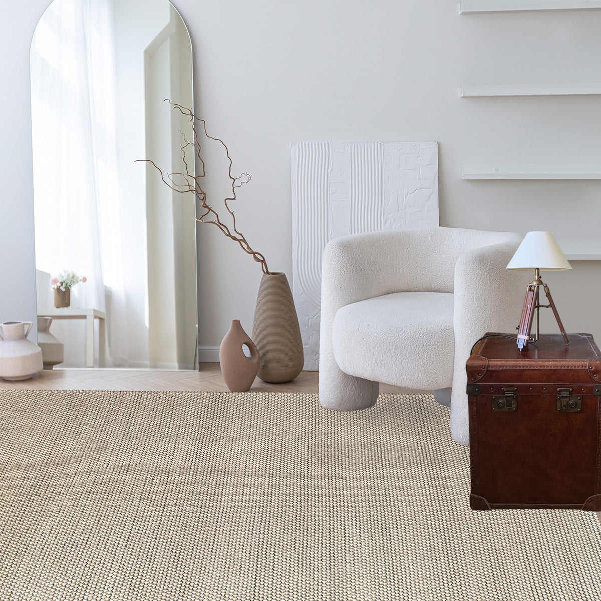 Beige loop rug in a white living room with a bouclé armchair, dark timber cabinet and a tall vase of branches