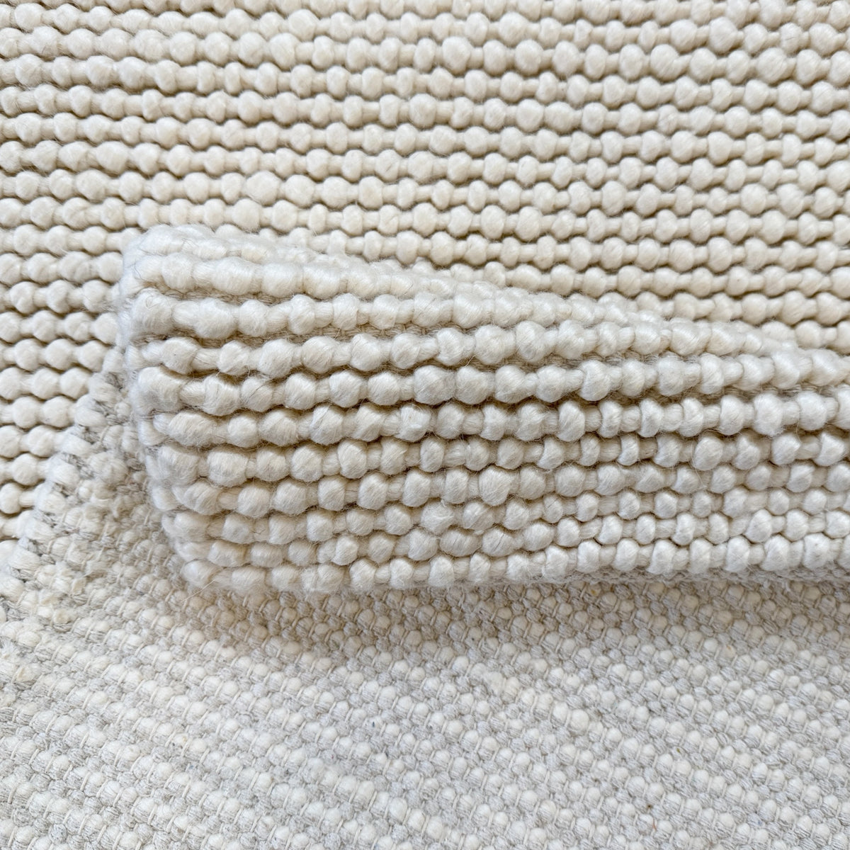 Folded corner of the ivory rug showing the loop pile and its underside