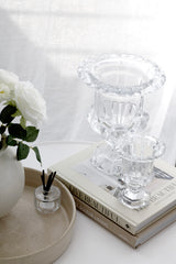 Clear glass urn vase with fluted bowl and pedestal base styled on books beside white flowers