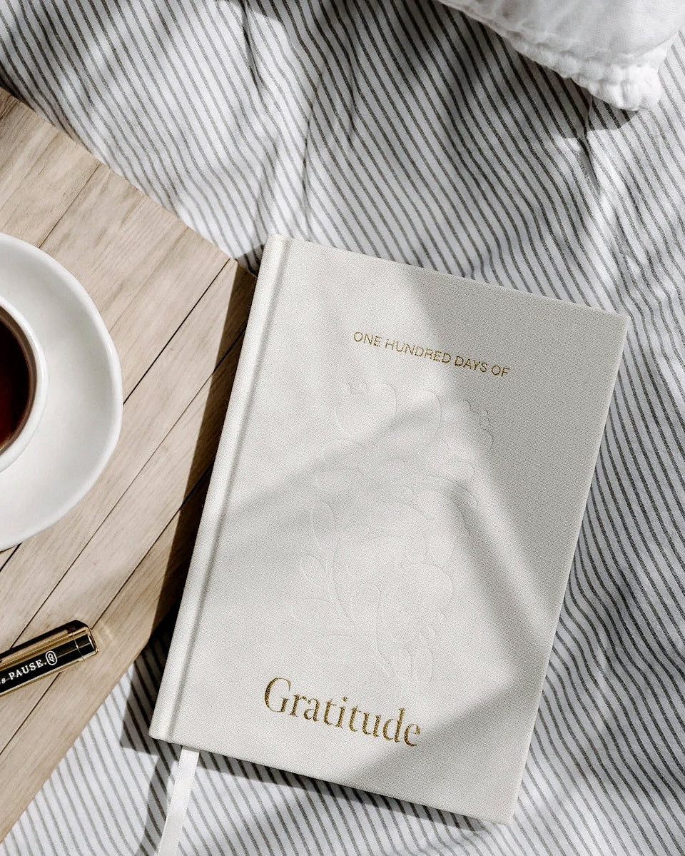 Gratitude journal on striped bedding beside a cup of coffee