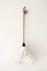 White ostrich feather duster with a beechwood handle and black cuff styled against a soft neutral wall.