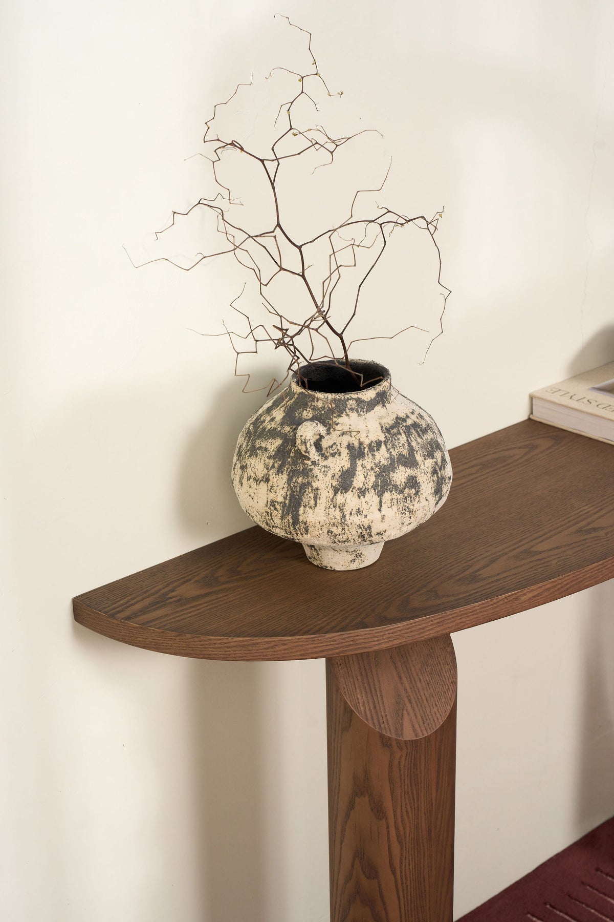 Curved end of the half-moon ash top with a speckled ceramic vase and branches