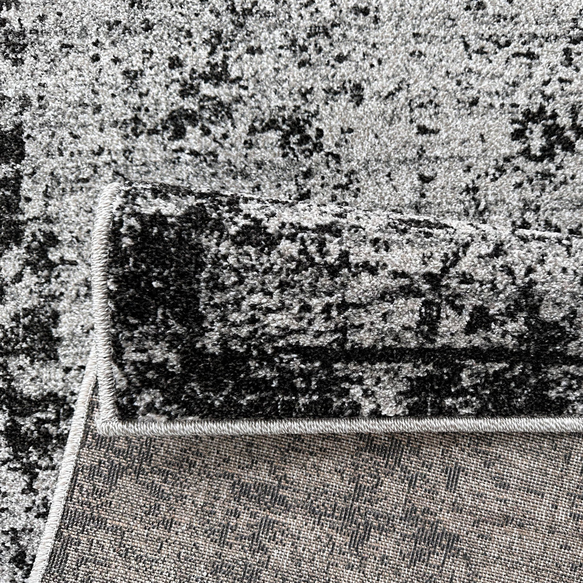 Grey and black rug folded back to show the woven backing