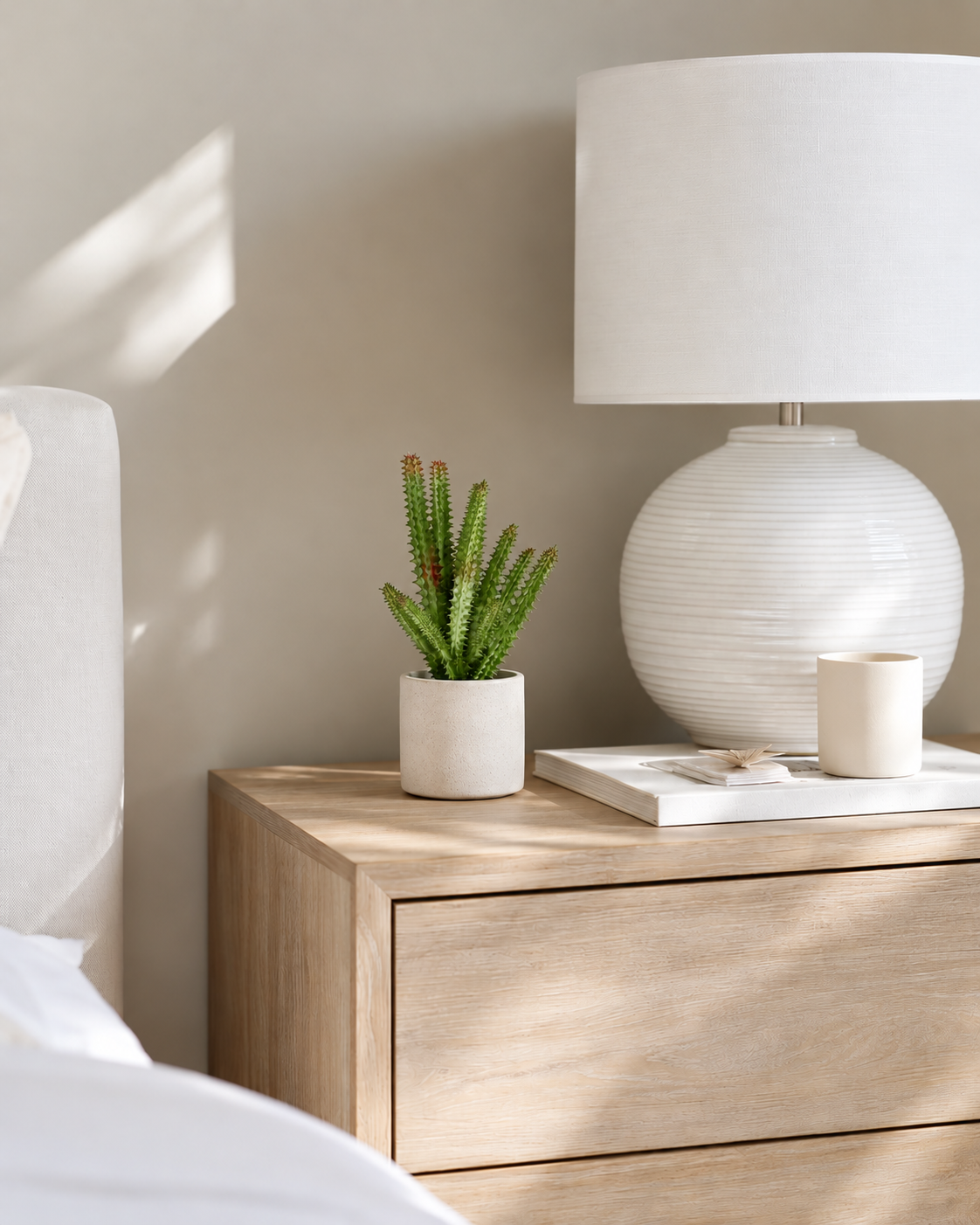Faux watch chain cactus in a small stone pot on an oak bedside table beside a white lamp
