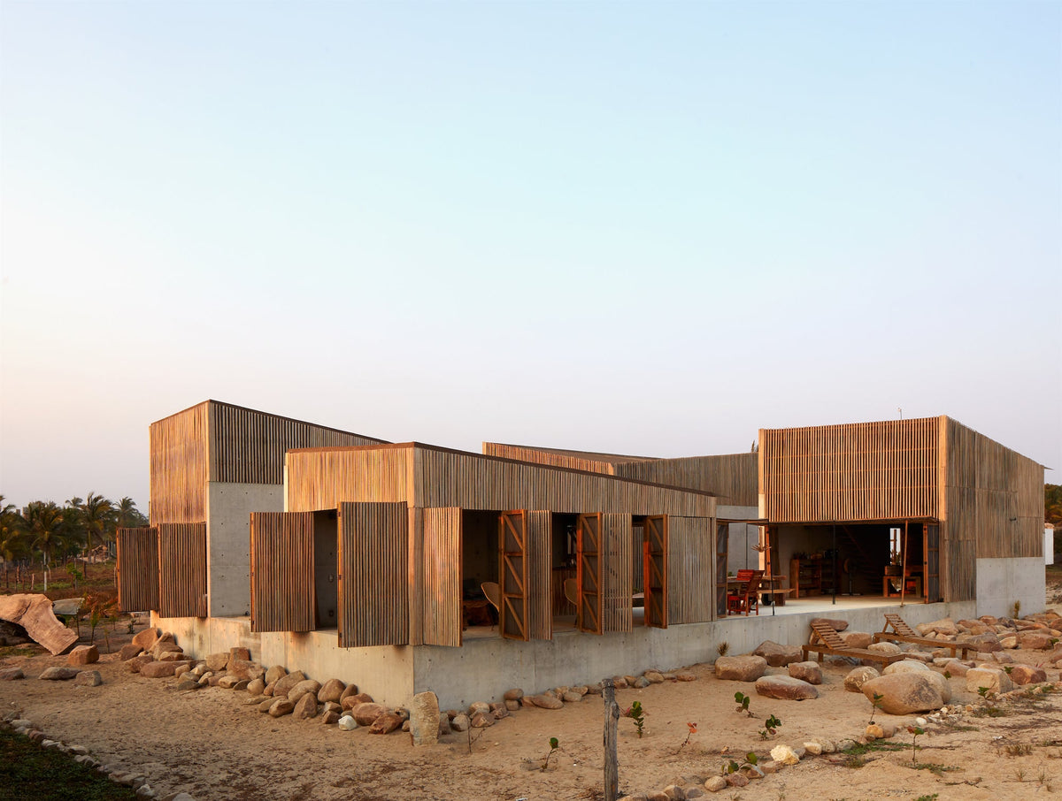 Photograph from Life's a Beach: a low timber-clad house on a rocky coastal site at dusk