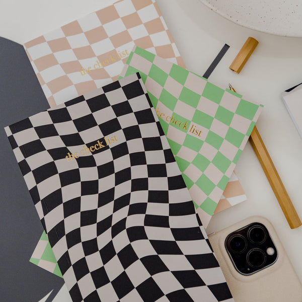 A THE CHECKLIST NOTEBOOK BLACK from Papier HQ in our stationary range on a table next to a phone.