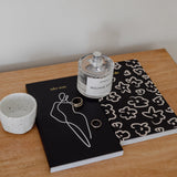 A limited edition HOMEBODII notebook and candle on a wooden table, from Papier HQ.