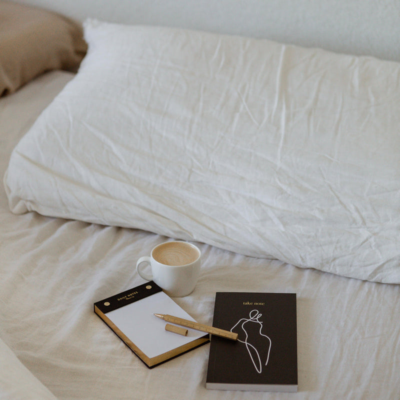 A limited edition HOMEBODII NOTEBOOK range by Papier HQ featuring lined notebooks placed on a bed with a cup of coffee.