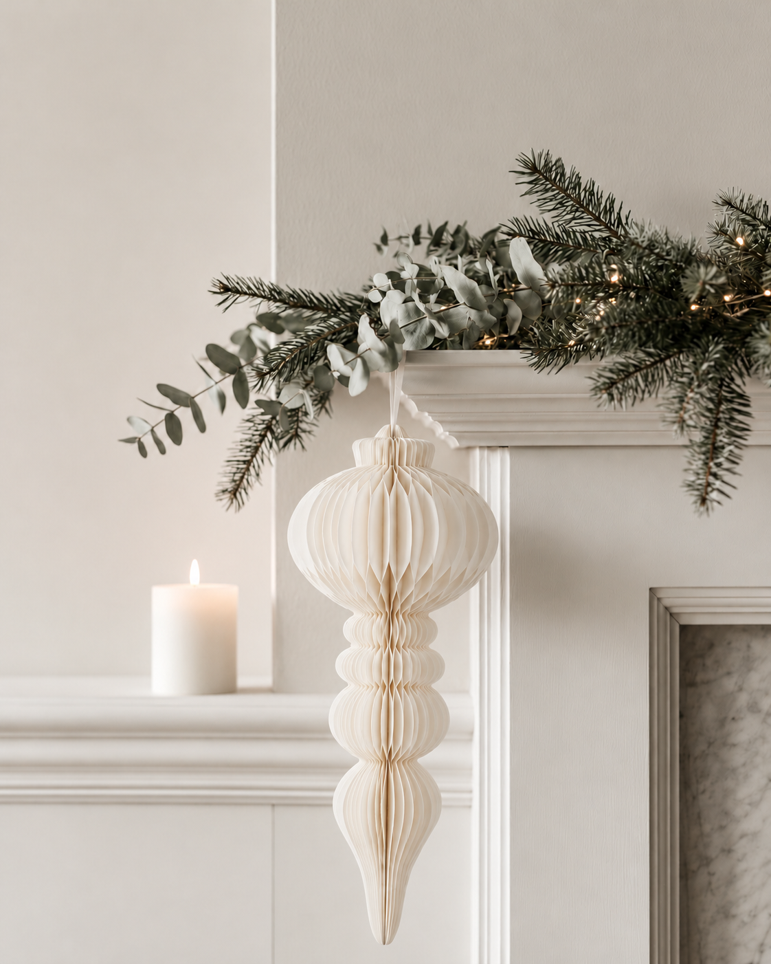 Papier Campana off white honeycomb paper decoration hanging from a mantel garland beside a white fireplace