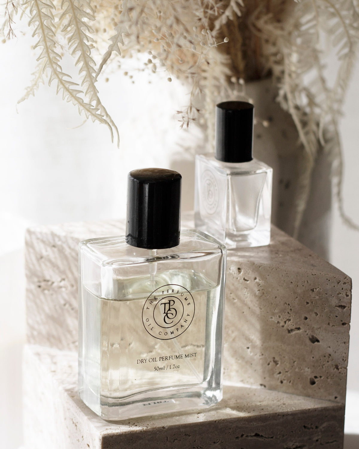Travertine bookends used as a plinth for two glass perfume bottles, dried fronds behind