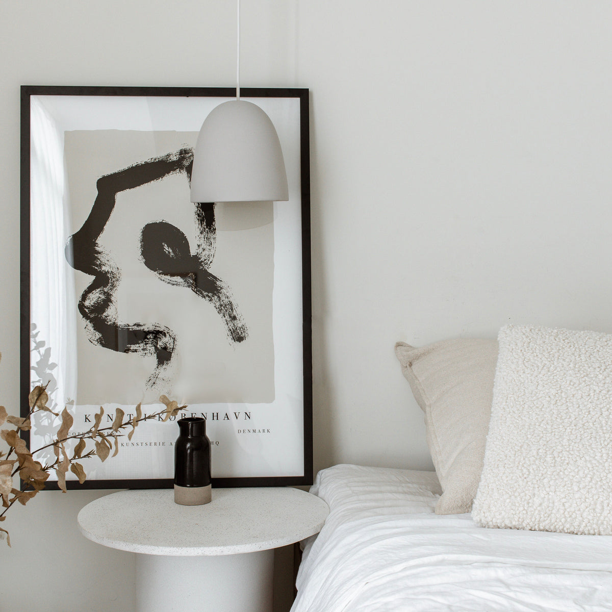 Copenhagen print in a black frame beside a bed and white side table under a pendant light