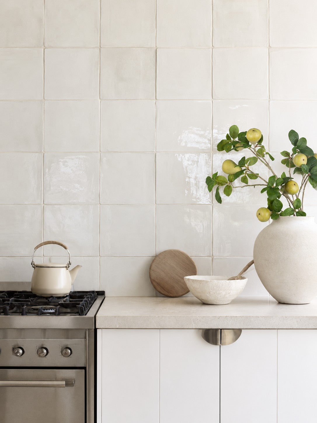 Faux pear branch spray in a white stoneware vase on a stone kitchen benchtop beside a ceramic bowl and wooden board