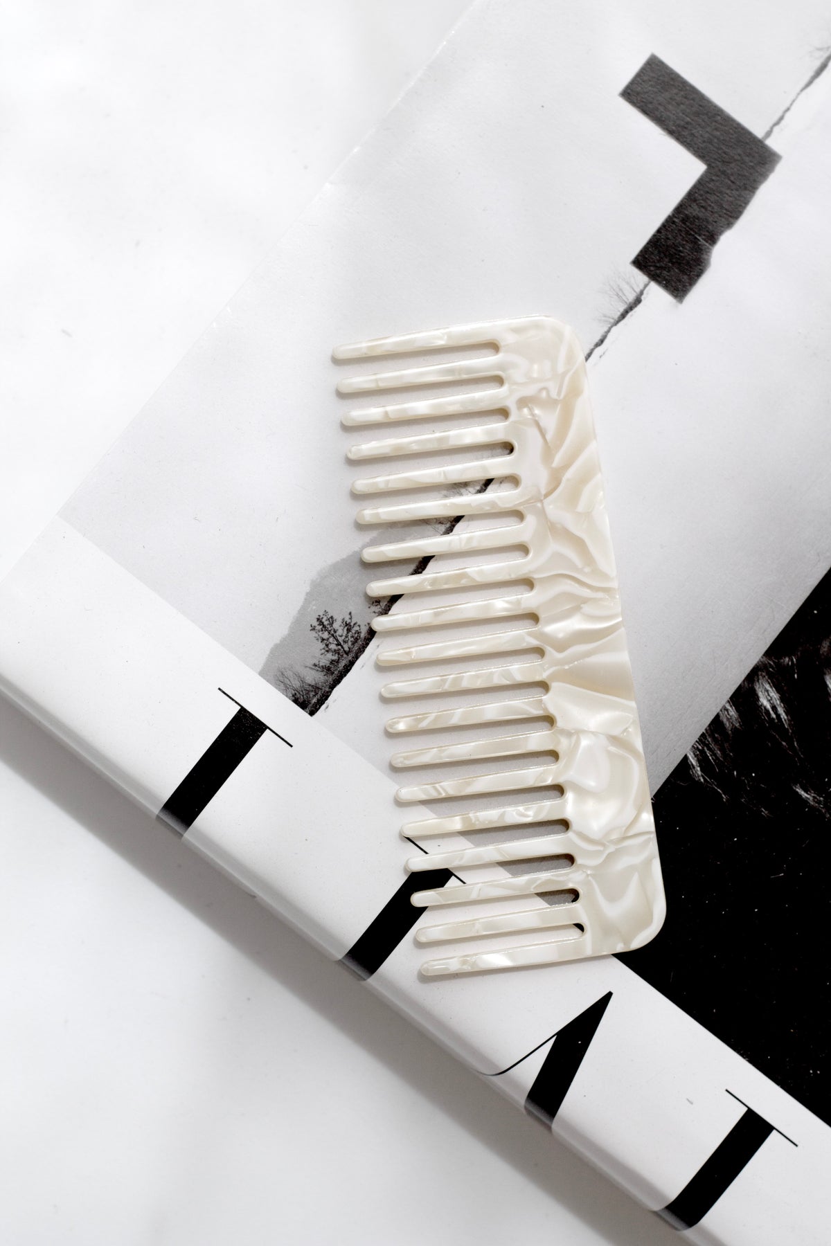 Pearl acetate comb on a monochrome hardback beside a slim black tube, flat lay
