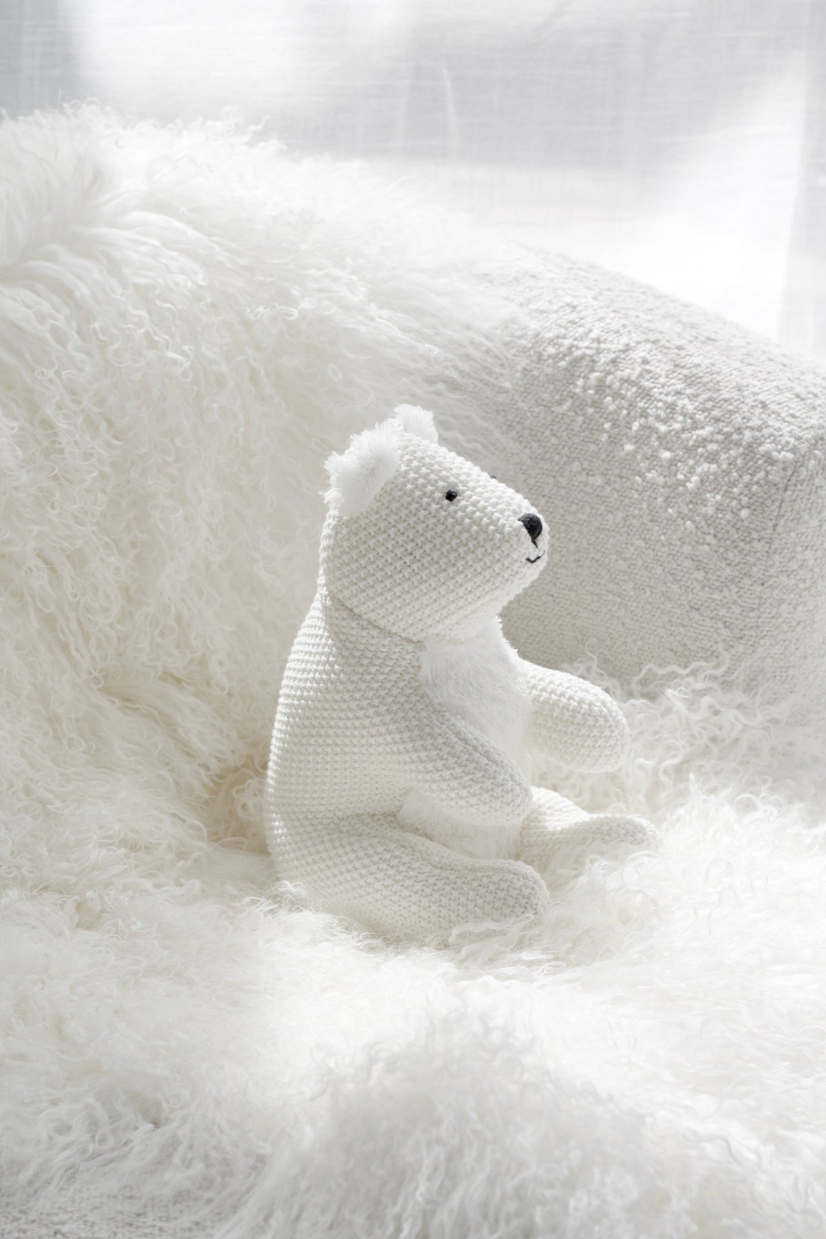Peter Polar Bear soft toy in knitted white fabric styled on a fluffy cream chair in a cosy neutral space.