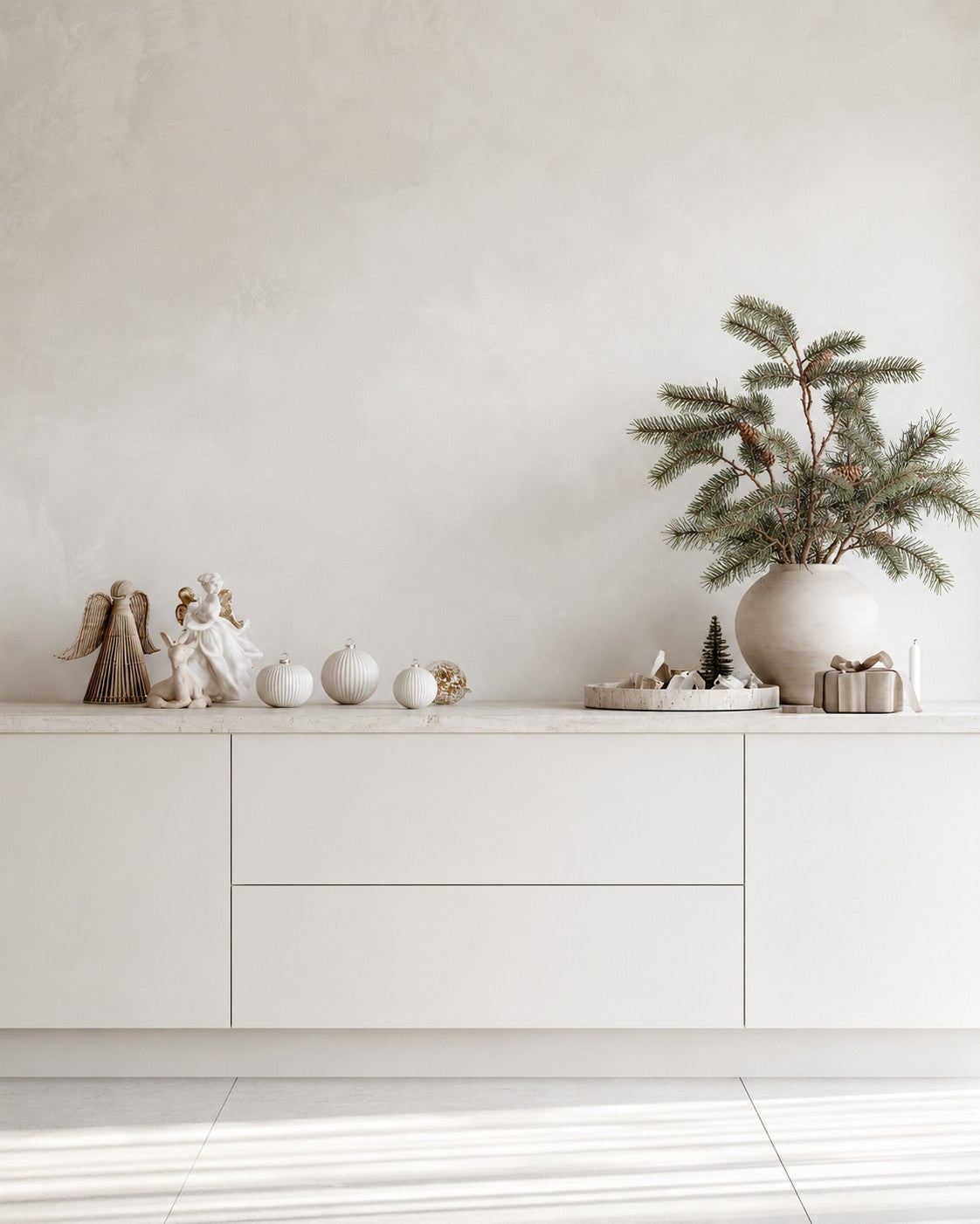 Faux pine branches with cones in a round stone vase on a white sideboard with Christmas decorations