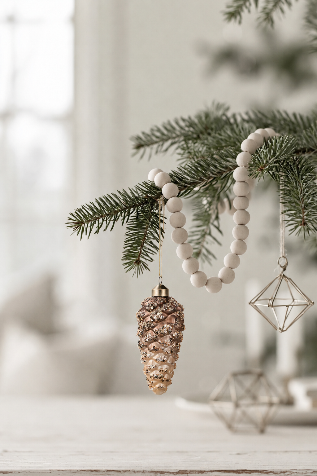 Pinecone Glass Bauble in brown 13cm hanging from a pine branch with a wooden bead garland and a geometric ornament
