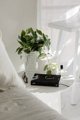 Artificial pothos variegated hanging bush styled in a textured clear glass vase on a bedside table.