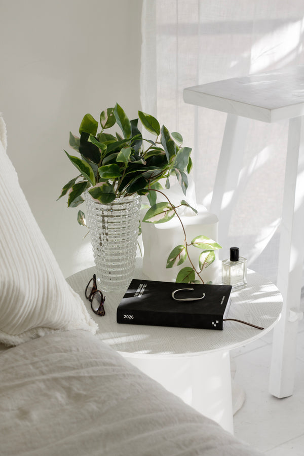 Artificial pothos variegated hanging bush styled in a textured clear glass vase on a bedside table.