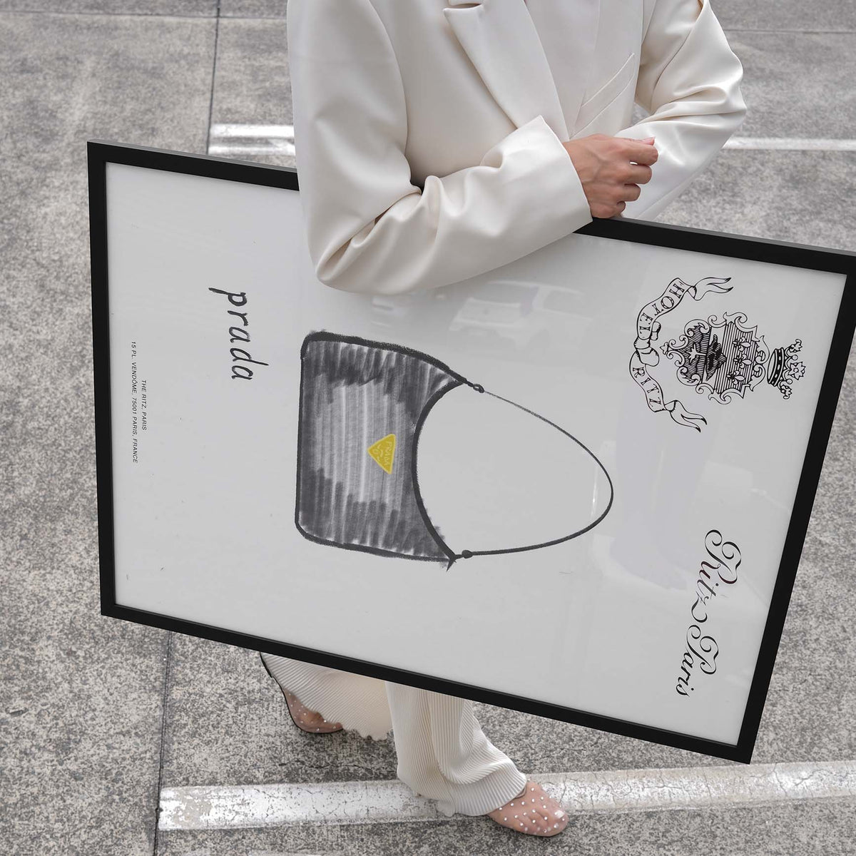 Person carrying the Prada Handbag print in a black frame across a car park