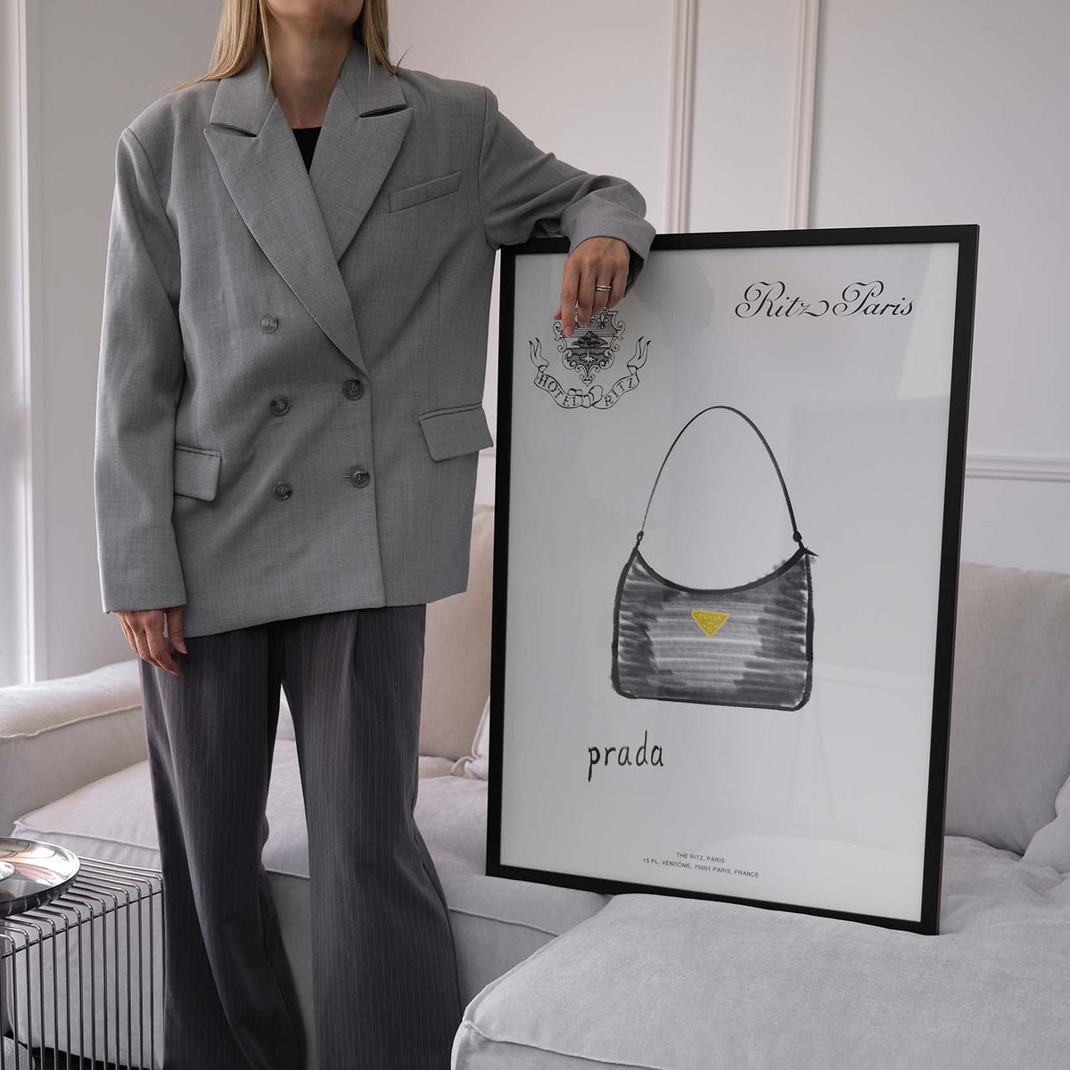 Woman in a grey suit standing beside the Prada Handbag print in a black frame on a sofa