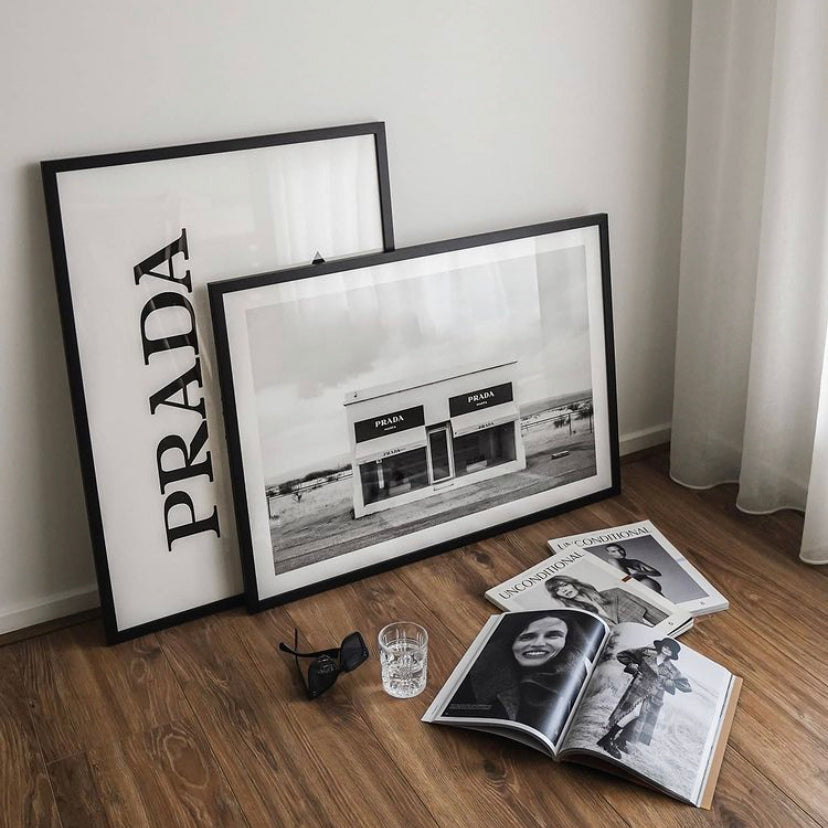 Prada Marfa print in a white frame leaning on timber floors beside the Marfa print and magazines