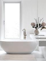 A modern bathroom with a freestanding white tub, minimalist fluted wall panels, and a sculptural artificial protea arrangement in soft peach and pink tones styled in a ceramic vase on a floating marble vanity.