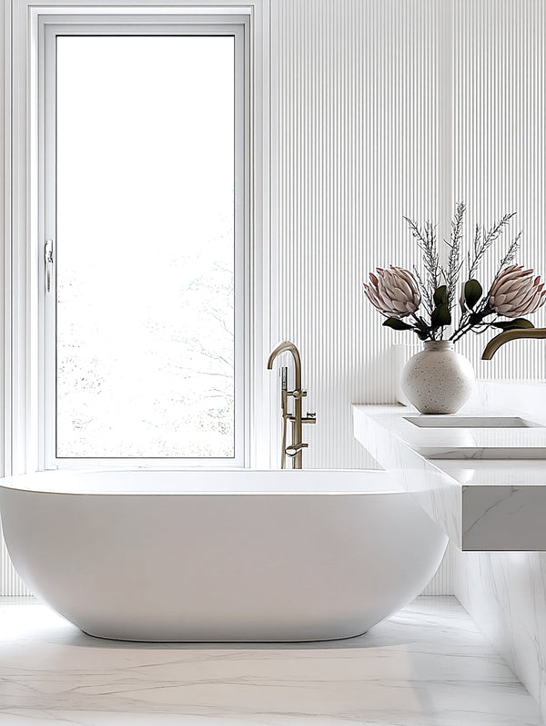 A modern bathroom with a freestanding white tub, minimalist fluted wall panels, and a sculptural artificial protea arrangement in soft peach and pink tones styled in a ceramic vase on a floating marble vanity.