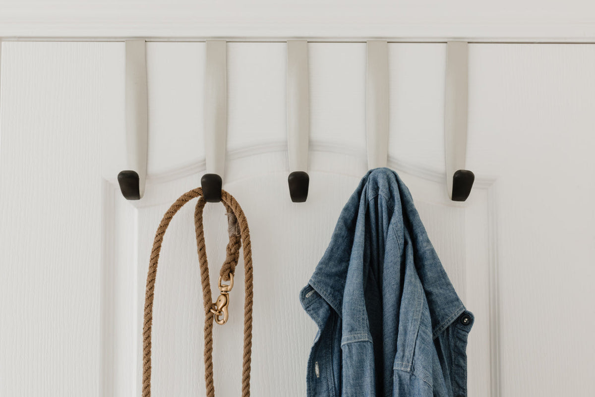Umbra Schnook five hook rail over a white door holding a jacket and a rope bag