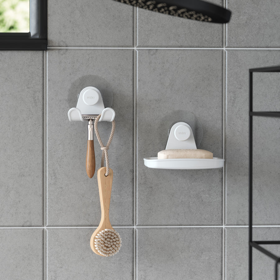Umbra Flex adhesive soap dish on grey tiles beside a hook with a body brush