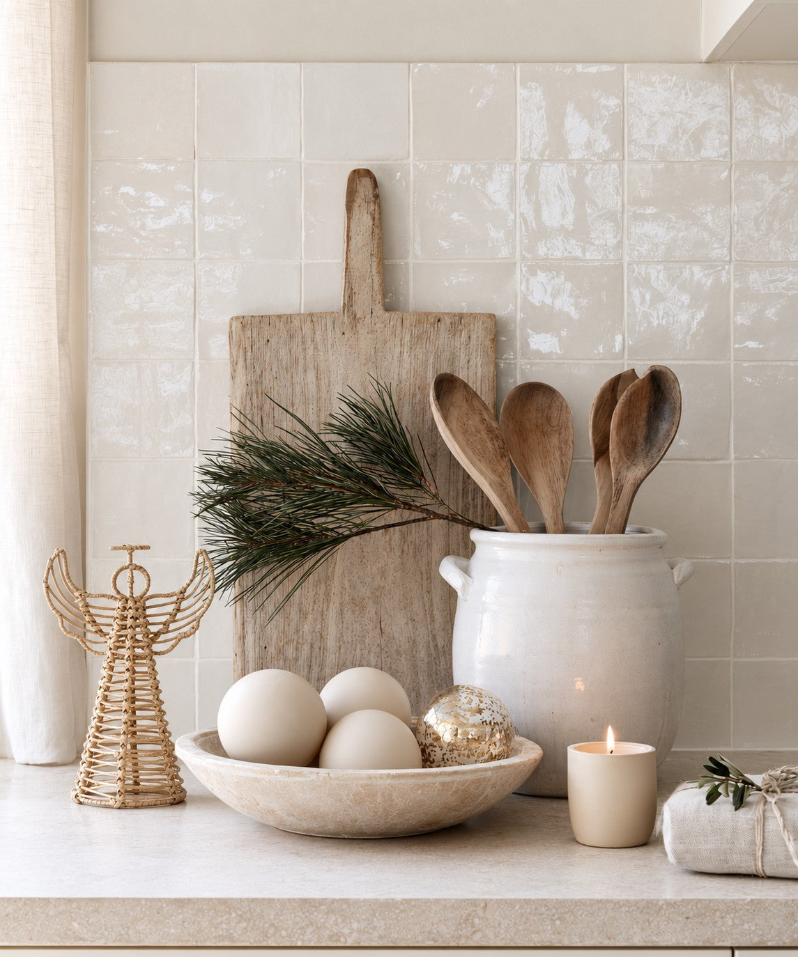 Rattan Christmas angel on a kitchen bench beside a bowl of baubles, a wooden board and a spoon crock