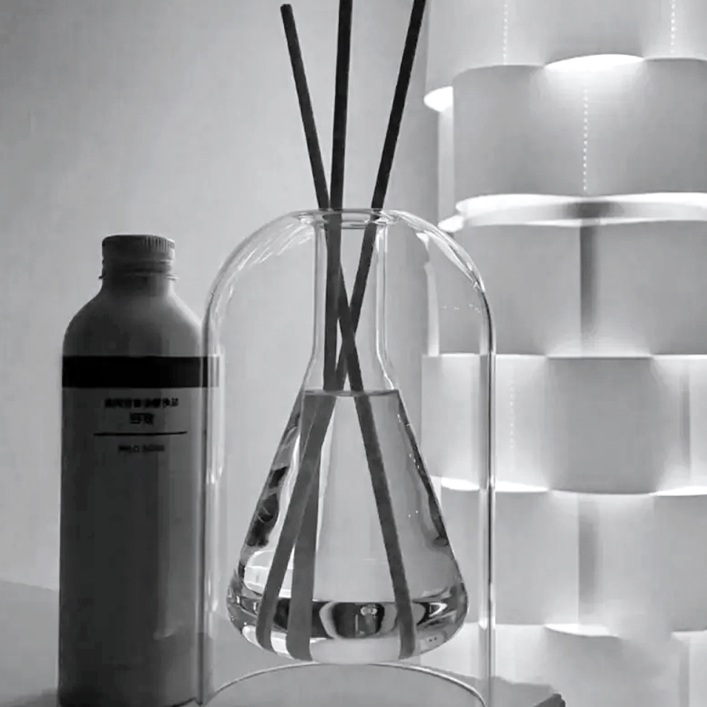 Black and white shot of the glass reed diffuser with dark reeds beside a refill bottle