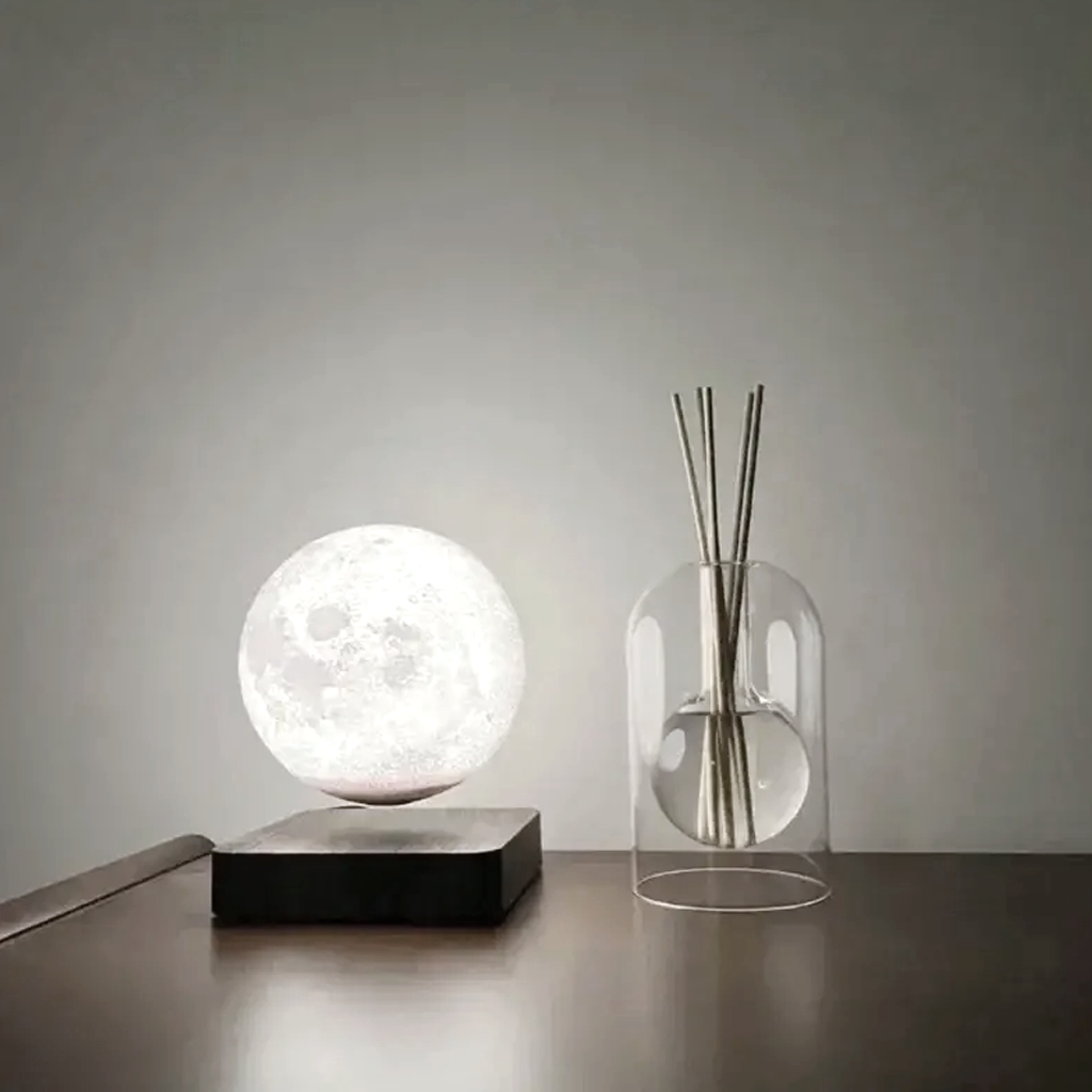 Glass reed diffuser on a timber sideboard beside a glowing round moon lamp
