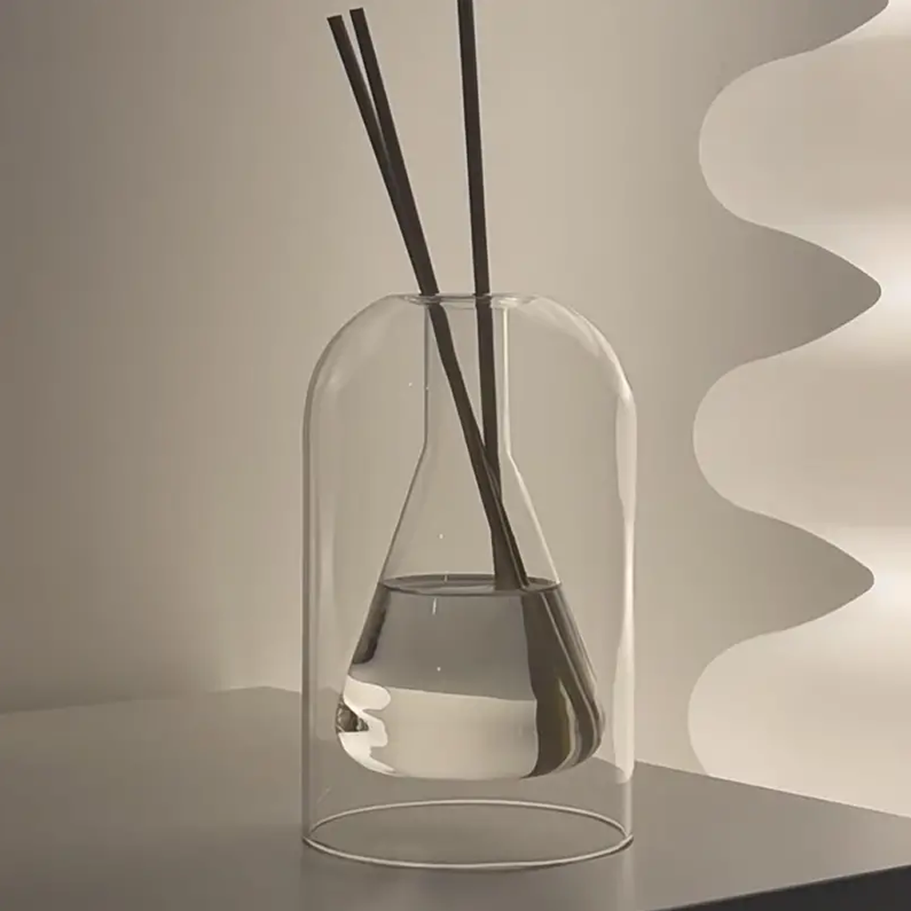 Glass reed diffuser with dark reeds on a shelf against a fluted cream wall panel