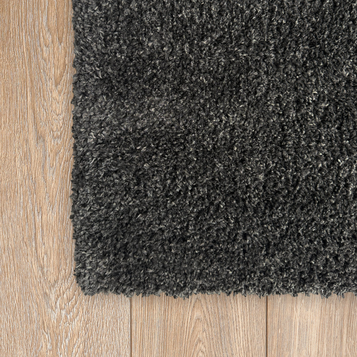 Corner of the charcoal plush rug on a pale oak floor