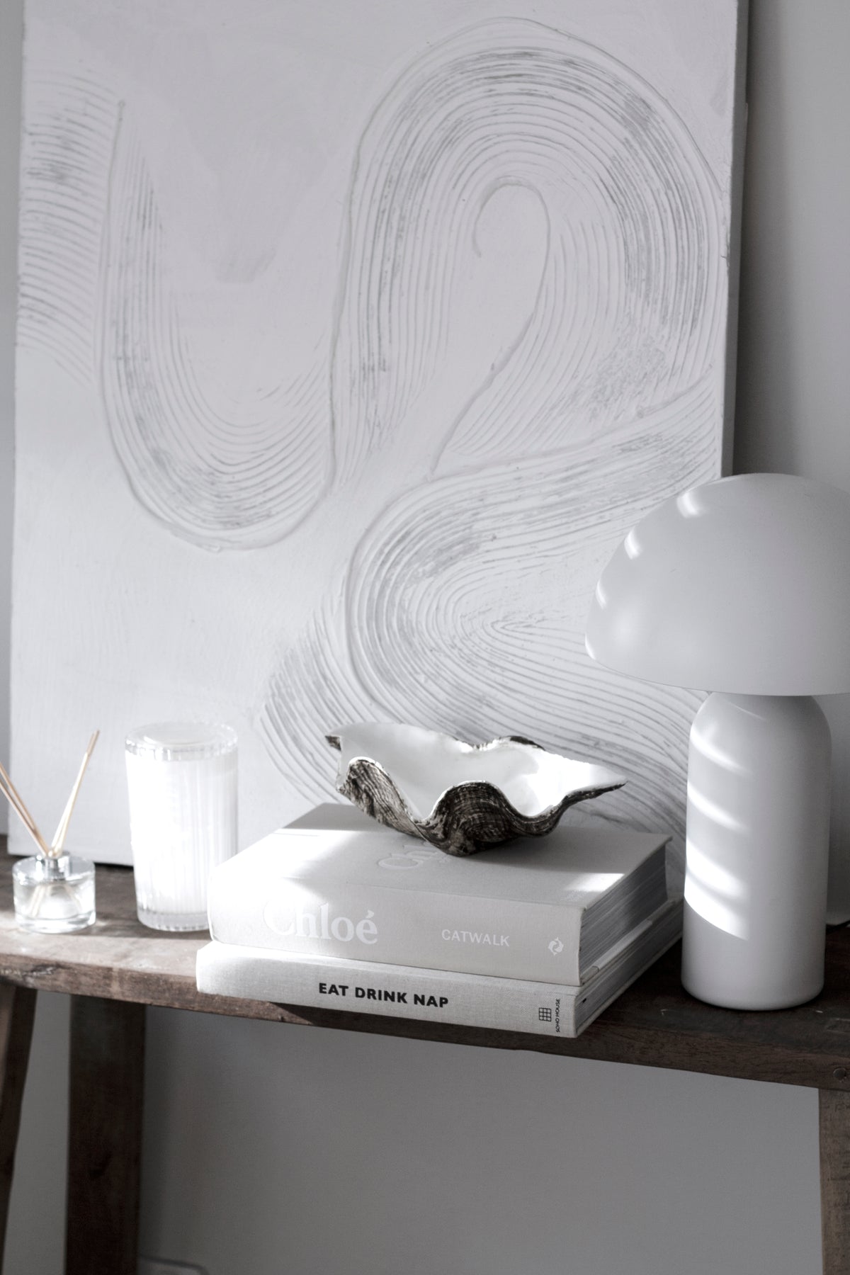 Resin clam shell bowl styled on books beside white table lamp in neutral coastal interior