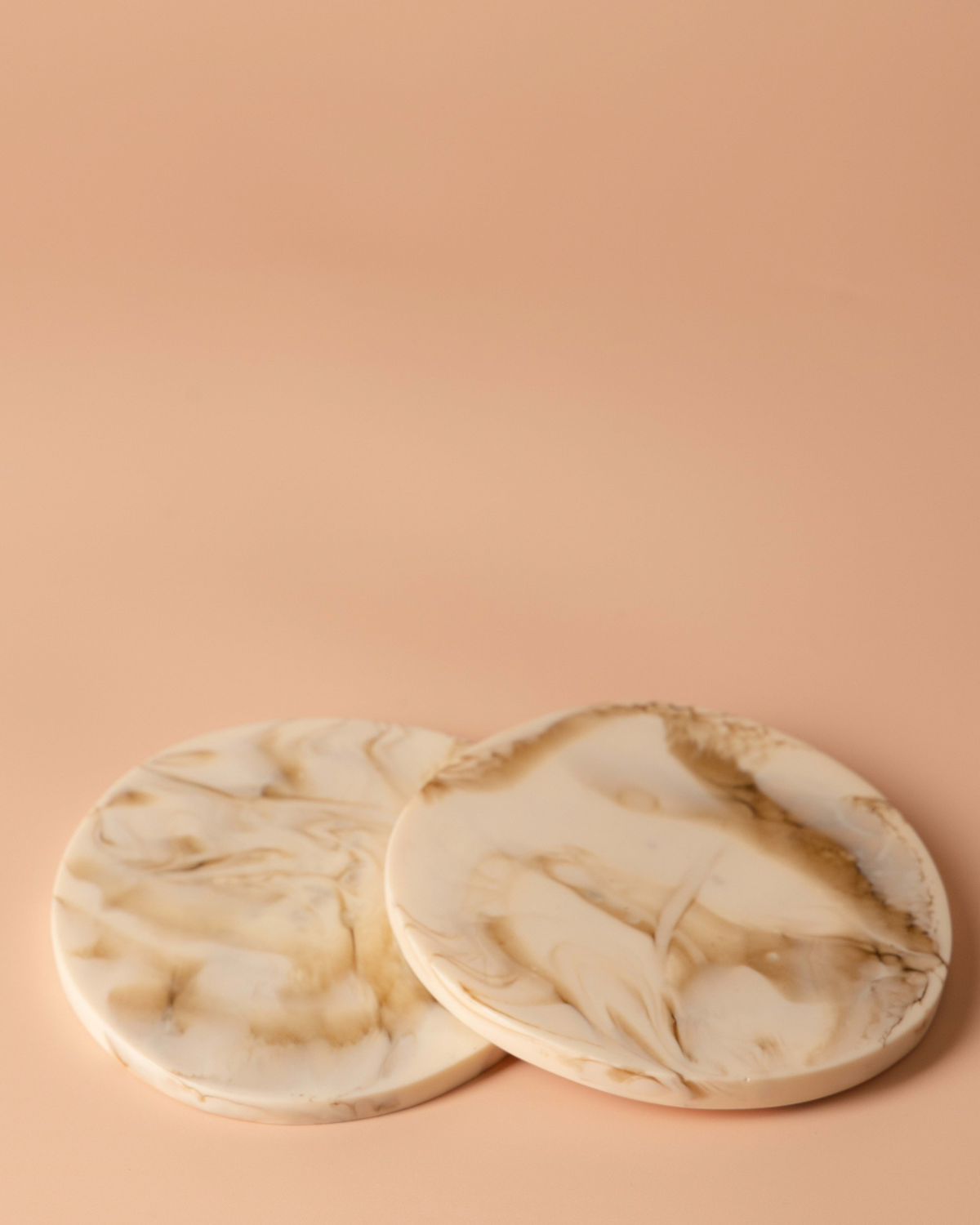Two Tiramisu resin coasters overlapping on a peach background, showing caramel swirls