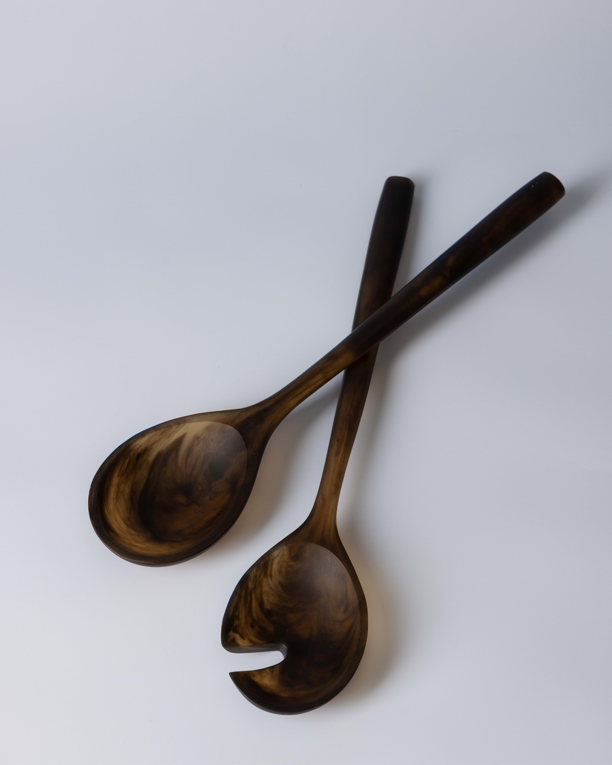 Chocolate resin salad servers crossed on a soft grey surface, showing marbled bowls and long handles