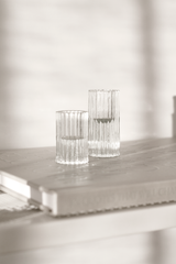 Set of two clear ribbed glass Ribb candle holders in different heights, styled on a neutral book in soft sunlight for minimalist home decor