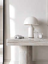 Ribbed glass tumbler with glass straw styled on travertine console with dome lamp and candle in minimal white interior