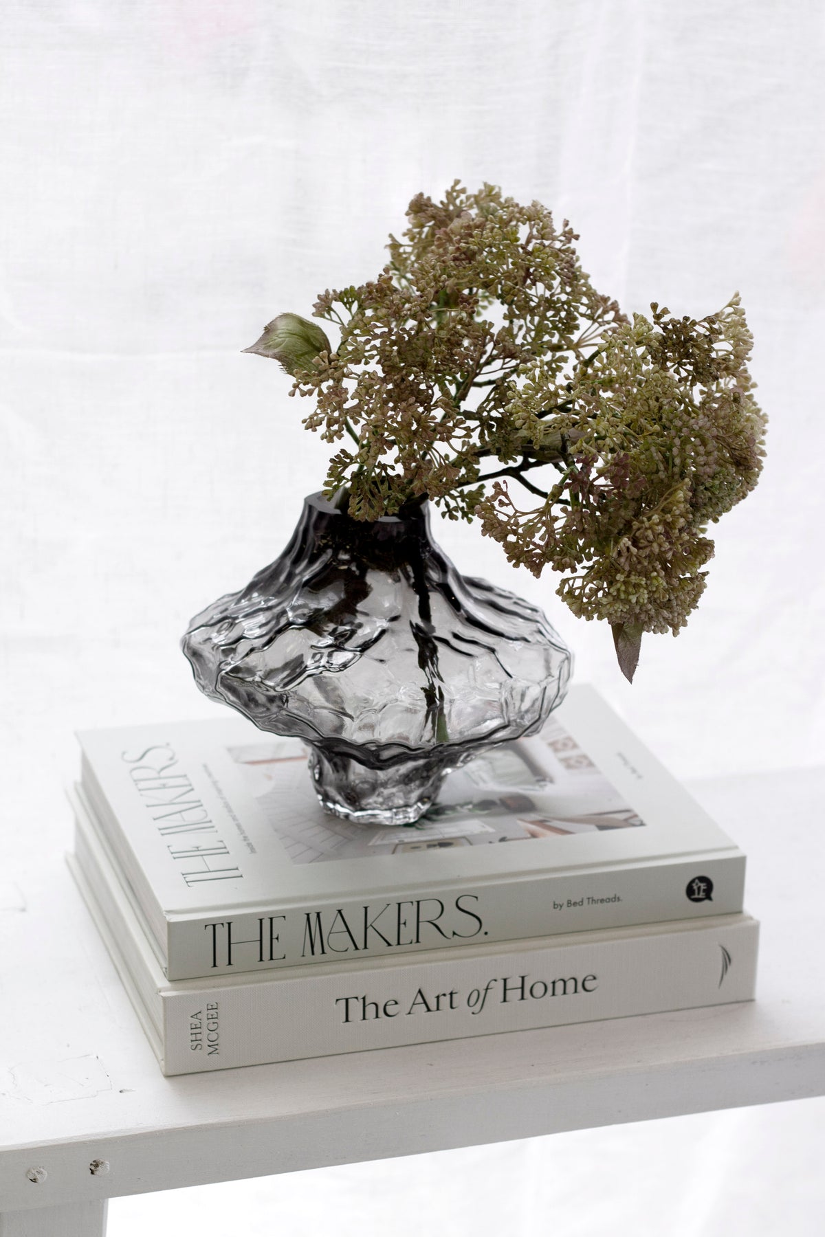 Smoky black rippled crystal glass vase holding dried hydrangea on a stack of styling books