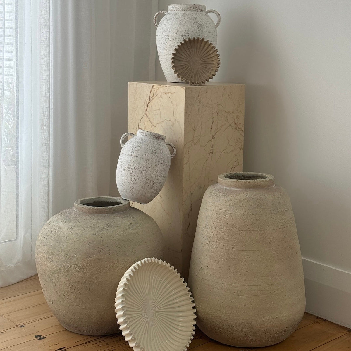 Rome scalloped platter on the floor beside textured stone vases and a plinth