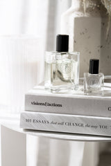 Square glass bottles of ROUGE perfume oil with black caps displayed on neutral books and a marble table, styled with natural light for a sophisticated, minimalist look.